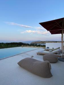 a patio with chairs and an umbrella and a pool at Amalthea, Outstanding Seaside Luxury Villa, Paros in Santa Marina
