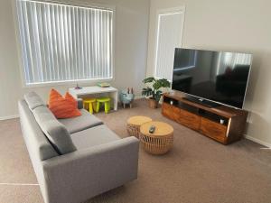 4BR House for Whole Family في Schofields: غرفة معيشة مع أريكة وتلفزيون بشاشة مسطحة
