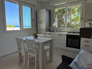 cocina con mesa blanca, sillas y ventanas en Beach Loft Poetto, en Quartu SantʼElena