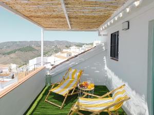 een balkon met 2 stoelen en een tafel met fruit erop bij Las Pizarrillas: tu hogar en este blanco pueblo in Frigiliana