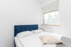 Cama blanca con cabecero azul y ventana en Apartamenty Mierzeja NCNK Baltic Twins Sztutowo, en Sztutowo
