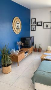 Il comprend un salon doté d'une télévision et d'un mur bleu. dans l'établissement La maison aux palmiers, à Arpaillargues-et-Aureillac