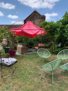 a group of chairs and a red umbrella in a yard at Charmant logement centre-ville in Houdan