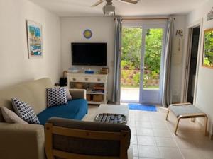 een woonkamer met een blauwe bank en een tv bij Bel Appartement avec Jardin pour 4 Personnes Climatisé avec Accès plage de la Gorguette à pied in Sanary-sur-Mer