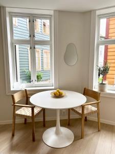 a white table and chairs in a room with two windows at Knøsesmauet Apartment in Bergen