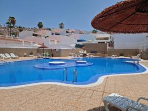 a large swimming pool with chairs and an umbrella at In the garden in Adeje