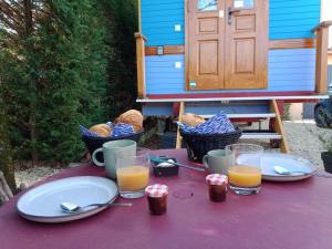 een paarse tafel met borden en glazen sinaasappelsap bij Roulotte jusqu'à 2 personnes Le Temps d une Pause en face du Beaujolais - Climatisation et Borne recharge véhicule électrique in Montmerle Sur Saône
