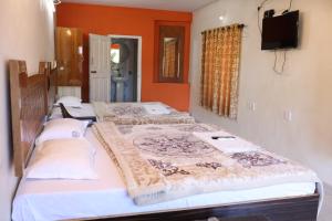 três camas num quarto com paredes cor de laranja e uma televisão em Hotel Sri Balaji em Ooty