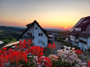 une maison avec des fleurs rouges devant un coucher de soleil dans l'établissement Renatas Ferienwohnung Sasbachwalden, à Sasbachwalden
