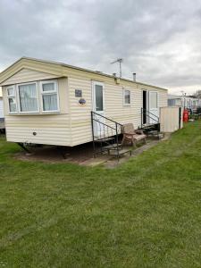 ein kleines gelbes Haus mit einer Veranda und einer Bank in der Unterkunft Caravan Holiday home Happy days south 17 in Chapel Saint Leonards