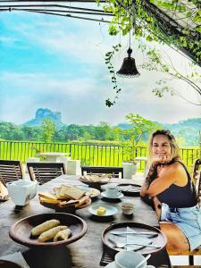 a woman sitting at a table with food on it at Kashyapa Kingdom View Home in Sigiriya