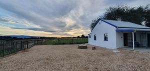 a small white building with a fence in a field at Karoo Leeu Cottage in Oudtshoorn