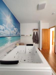 a white bath tub in a room with a painting of the ocean at Casa Airen con jacuzzi in Miguel Esteban