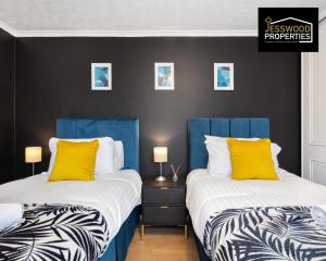 2 camas en una habitación con almohadas azules y amarillas en Stylish 3 Bedroom Contractor House Stevenage by Jesswood Properties Short Lets Free Parking & Wifi en Stevenage