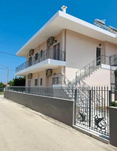 a white building with stairs and a fence at Koulouras Holiday Apartments in Nikolaíika