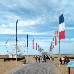 a boardwalk with flags and a ferris wheel on the beach at Appartement Ouistreham proche centre et plage in Ouistreham