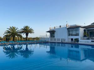a large swimming pool with palm trees and a building at Beach House Golden Club in Cabanas de Tavira