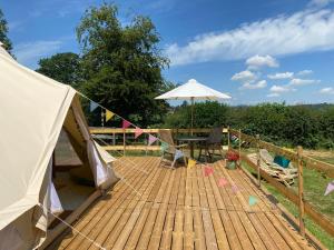 une terrasse en bois avec une table et un parasol dans l'établissement Hope Cottage Bell Tent Retreat, à Ashbourne