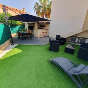 a backyard with a green lawn with chairs and an umbrella at Joli haut de villa 3 chambres climatisé avec jacuzzi in Marignane