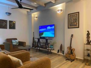 ein Wohnzimmer mit einem Sofa, einem TV und einer Gitarre in der Unterkunft Hibiscus Home Stay & Boutique in Port Blair