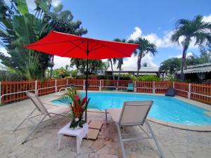 a red umbrella and two chairs next to a pool at ISK LOCATION in Sainte-Rose