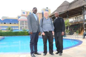 three men standing next to a swimming pool at Fatima Hotel in Ruhengeri