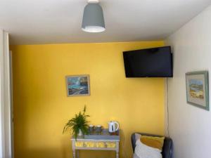 a room with a yellow wall with a flat screen tv at Light airy comfy small double room with en-suite in Falmouth