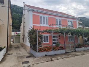 a pink and white house with flowers in a courtyard at Apartman Anka in Komin