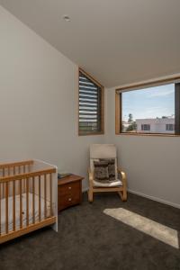 a bedroom with a crib and a chair and a window at Twin Peaks Beach House - New Plymouth Holiday Home in New Plymouth