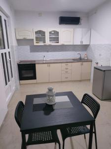 une cuisine avec une table et des chaises noires et une cuisine avec des armoires blanches dans l'établissement Apartman Milenkovic, à Malo Laole