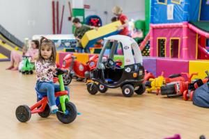 德布勒森的住宿－Szusz Szállás，一个小女孩在一间房间里骑玩具车,并带上其他玩具