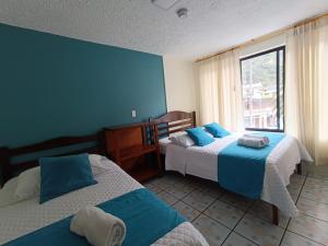 sypialnia z 2 łóżkami z niebieskimi ścianami i oknem w obiekcie Hostal CañaLimeña w Baños