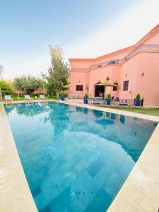 una piscina de agua azul frente a un edificio rosa en Villa ELIANA, en Marrakech