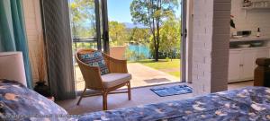 a bedroom with a bed and a chair and a large window at The Glade, peace among the trees on the river in Urunga