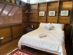 1 dormitorio con cama blanca y pared de madera en Kebun Lisdtari farmstay, en Air Hangat