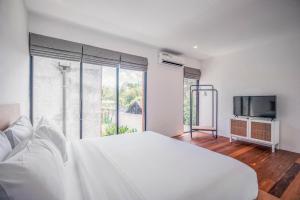 Un dormitorio blanco con una cama grande y un televisor. en Umalas Living Villa, en Canggu