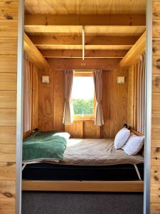a bed in a wooden room with a window at Margo's Garden Farmstay, Kiroro in Akaigawa