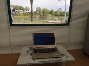 un computer portatile seduto su un tavolo di fronte a una finestra di Buasawan Resort & Restaurant a Kanchanaburi