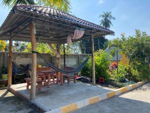a picnic shelter with a hammock and a table and bench at Lazy Mango Home Stay in Phumĭ Poŭthĭ Mâ Srei