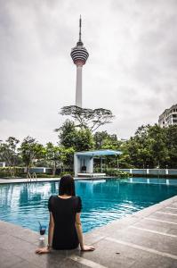 a woman sitting next to a pool with a tower in the background at Suasana Suites Bukit Ceylon in Kuala Lumpur