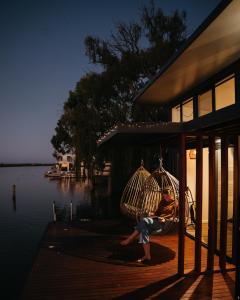 eine Person, die in einer Schaukel auf einer Veranda neben dem Wasser sitzt in der Unterkunft Ark-imedes - Unique float home on the Murray River in White Sands