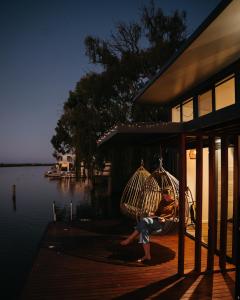 uma pessoa sentada num baloiço num alpendre junto à água em Ark-imedes - Unique float home on the Murray River em White Sands