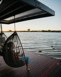 a child sitting in a hammock on a dock near the water at Ark-imedes - Unique float home on the Murray River in White Sands