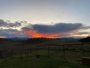 um pôr-do-sol sobre um campo com uma cerca e montanhas em Twin peaks em Underberg