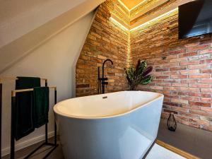 a white bath tub in a bathroom with a brick wall at Apartament Zielone Fotele Starówka in Olsztyn