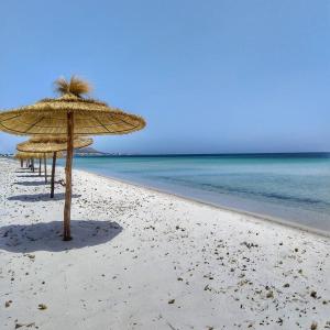 two straw umbrellas on a beach with the ocean at Dar Bhar in Kelibia