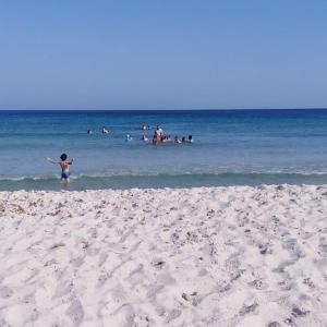 a girl standing on a beach with people in the water at Dar Bhar in Kelibia