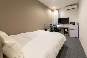 Habitación de hotel con cama blanca y escritorio en HOTEL R9 The Yard Ishioka, en Ishioka