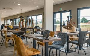 une cafétéria avec des tables et des chaises dotées d'un ordinateur portable dans l'établissement The Originals City, Relais d'Estillac, Agen Sud, à Estillac