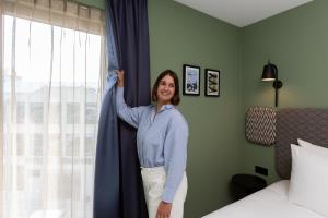 a woman standing next to a window with a curtain at Aparthotel Timmerfabriek Apartments I Kloeg Collection in Vlissingen
